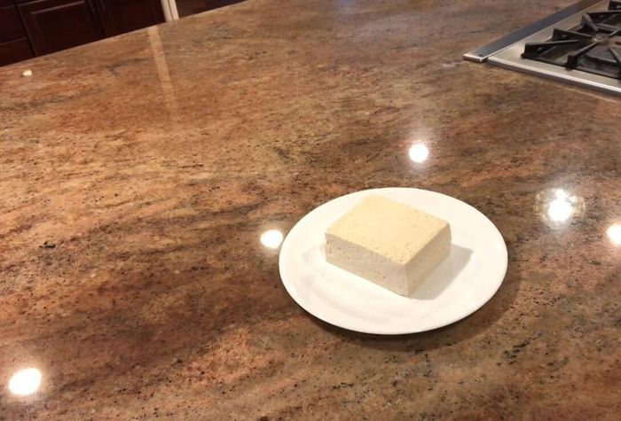 Remove tofu from packaging and pat it dry with several layers of paper towels. Create a package-like structure with the paper towels, enclosing the tofu.