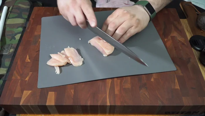 Knife slicing chicken breast on cutting board