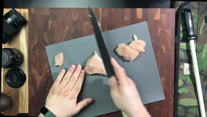 Knife slicing chicken breast on board
