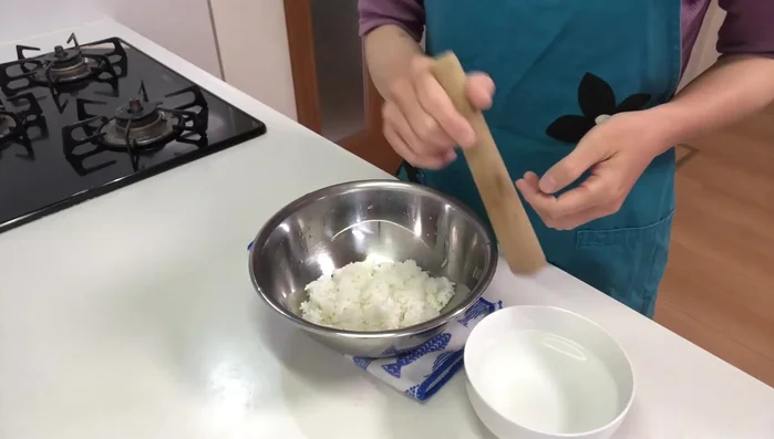Prepare Kiritampo: Pound cooked rice with a wooden pestle, adding salt water until it's well-mixed.