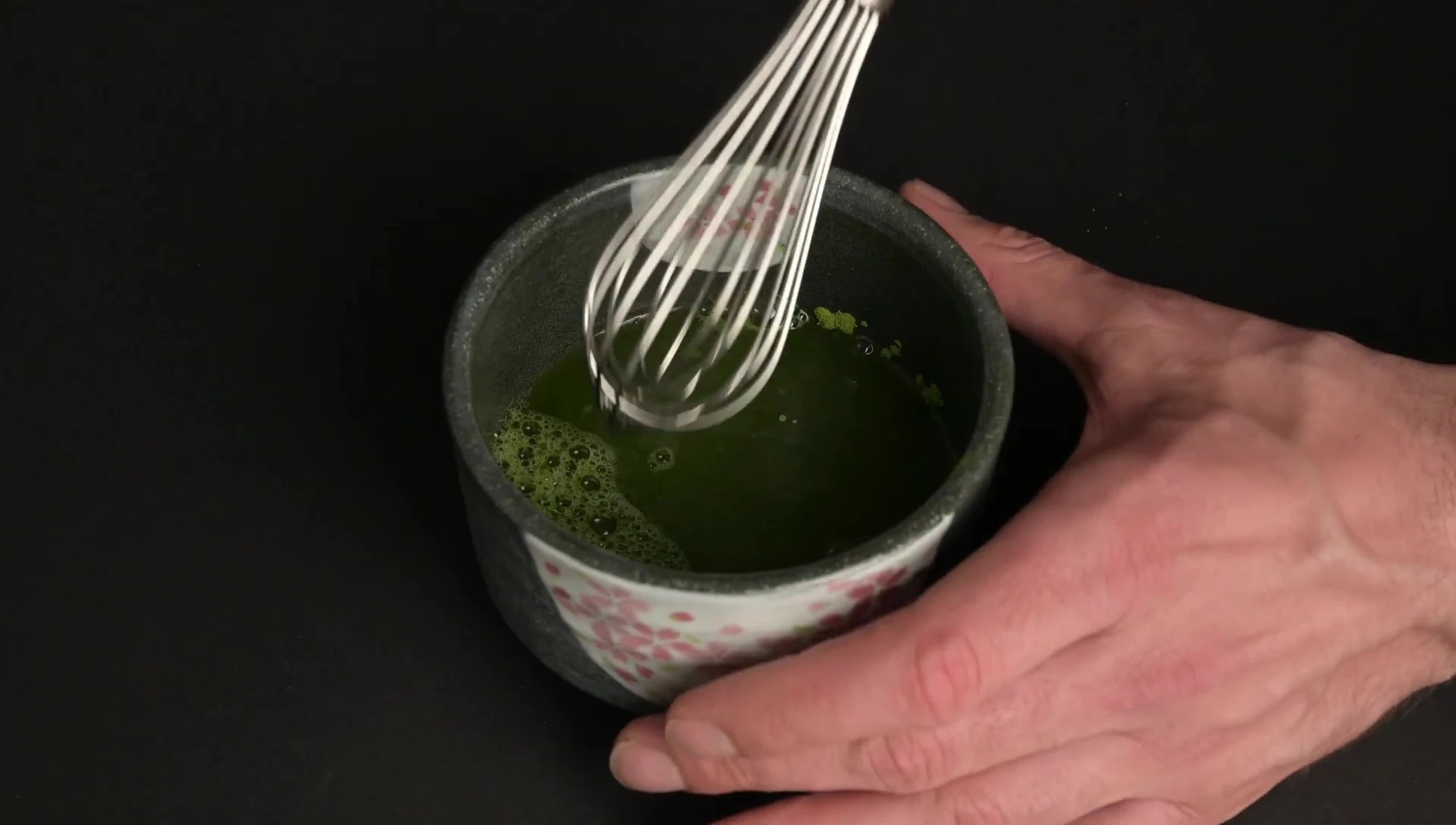 Metal whisk frothing matcha in bowl