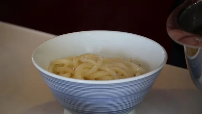 Assemble the udon: Drain noodles and place in bowls. Add broth, kamaboko, leek, and tempura bits. (224.159)
