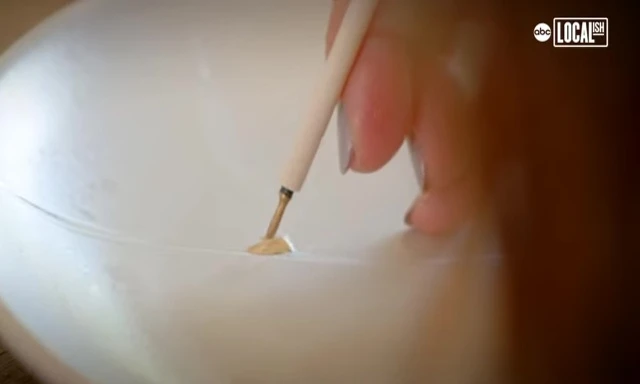 A woman demonstrating modern kintsugi techniques, showcasing the use of resin and brass powder.
