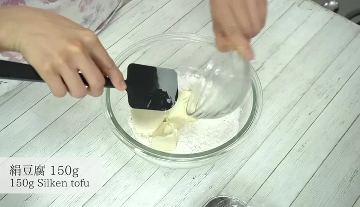 Add the silken tofu (undrained) and mash it while mixing until the dough becomes less fluffy and starts to clump together.