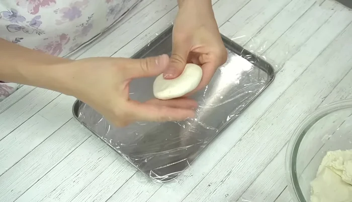 Take one dough portion, roll it into a ball, flatten it, and place a portion of sweet bean paste in the center. Wrap the bean paste tightly, sealing the edges.