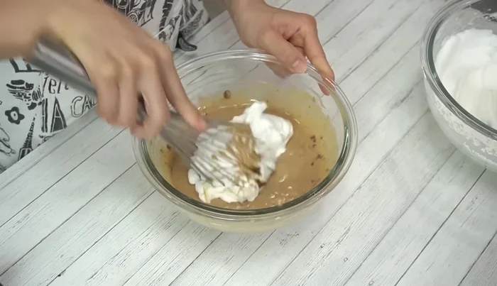 Gently fold the whipped egg whites into the egg yolk batter in two additions. The first addition should be mixed more thoroughly to combine the consistency. Subsequent additions should be mixed gently to avoid deflating the meringue.