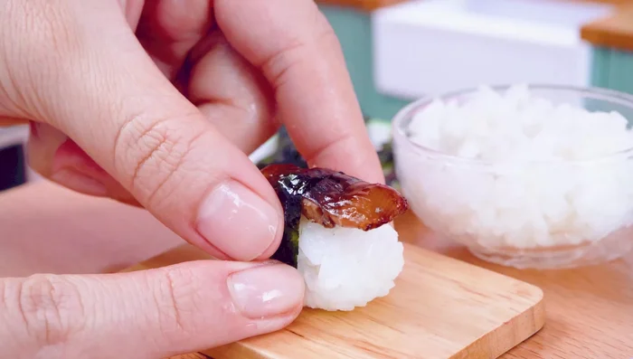 Assemble the eel sushi: Put eel on rice, top with seaweed.