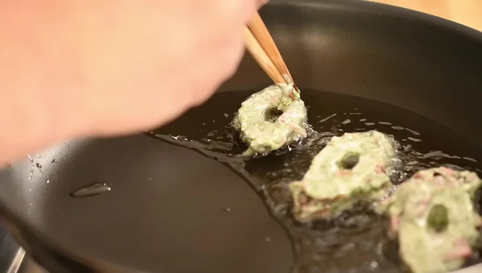 Carefully place the chikuwa in the hot oil, ensuring the batter doesn't clog the holes. Use chopsticks to adjust as needed.