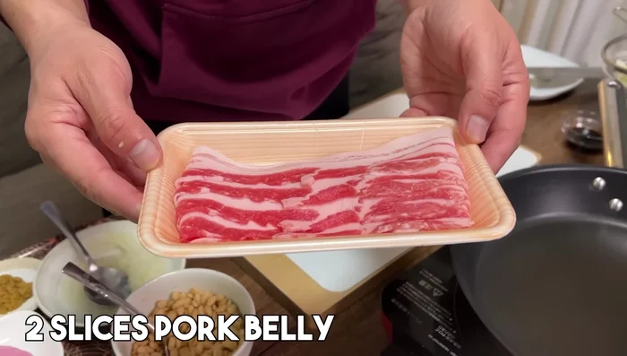 Cook pre-cooked udon noodles. Stir-fry onion and carrot until softened, then add cabbage and bell pepper. Add pork belly, udon noodles, instant dashi powder, soy sauce and mix well. Gently grill for a browned texture. Add toppings like bonito flakes.