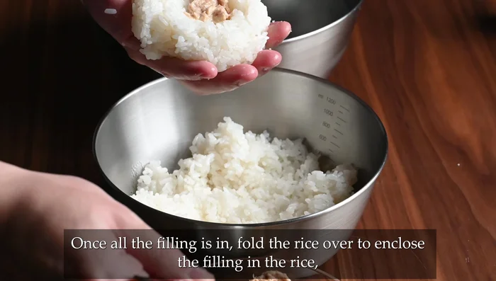 Add 2 tsp tuna mayo to the rice dent. Fold the rice over the filling, pressing and shaping it into a triangle.