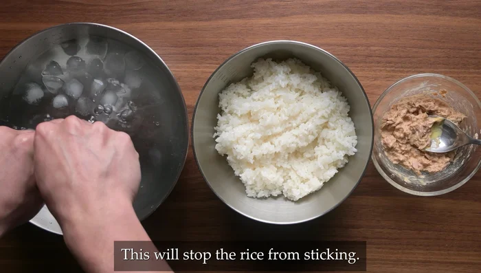 Dip hands in cold water and rub with salt. Grab 100-120g rice, press it into your palm, and make a dent in the center.