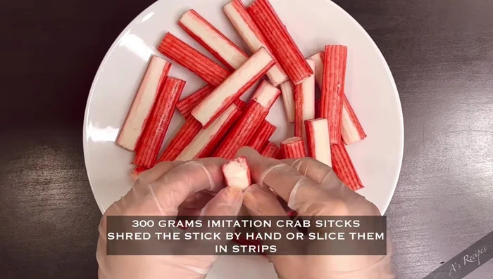 Shred or slice 300 grams of imitation crab sticks into strips and add them to a mixing bowl.