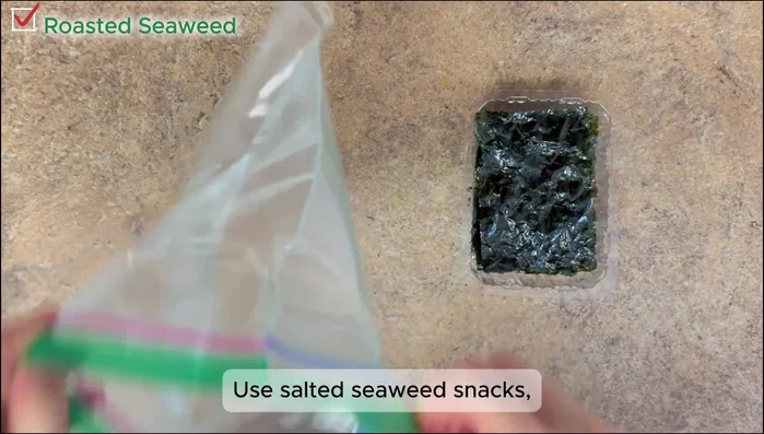 Prepare seaweed flakes by crushing salted seaweed sheets in a plastic bag.