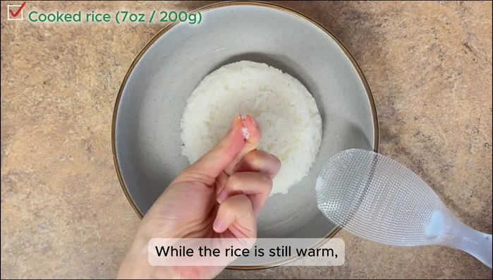 Mix warm cooked rice with salt, oil, and sesame seeds. Use the edge of a spoon to avoid mashing.