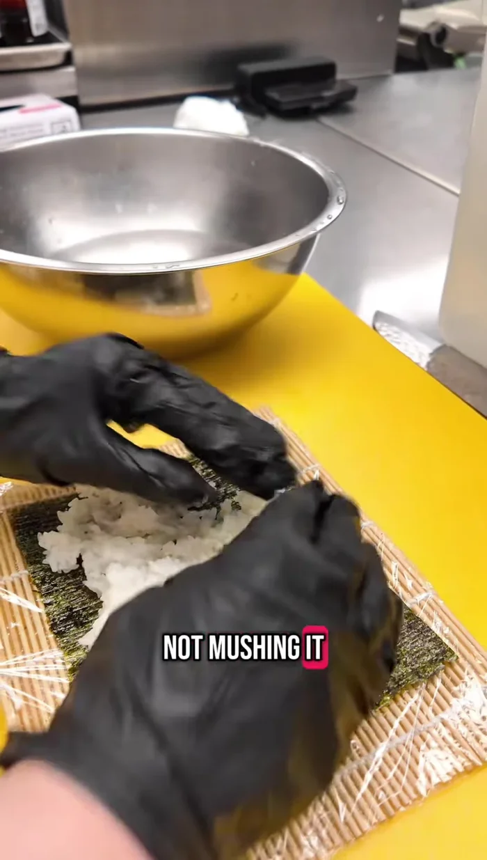 Wet your hands and gently place rice onto the saran-wrapped sushi mat, leaving a small overhang.
