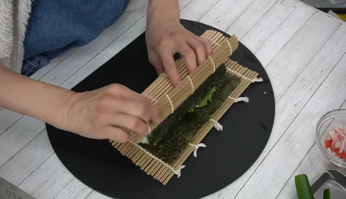 Roll tightly: Fold the end of the nori over the filling, and roll firmly. Secure with a rubber band and let it rest for 10 minutes.