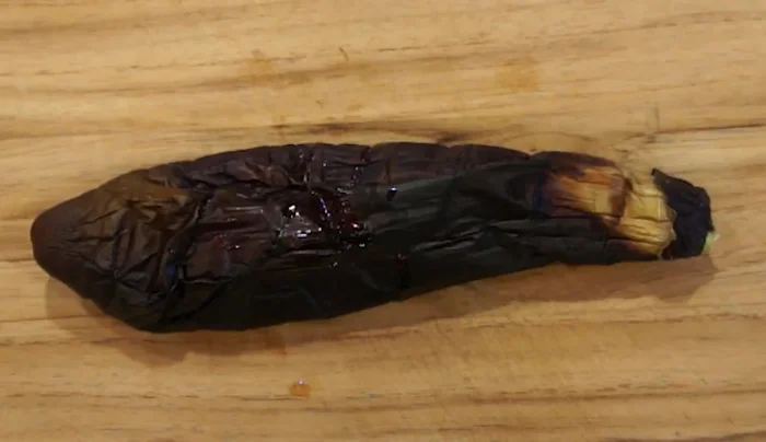 Remove the eggplants from the heat and let them cool slightly. Then, peel off the skin using a skewer or toothpick.
