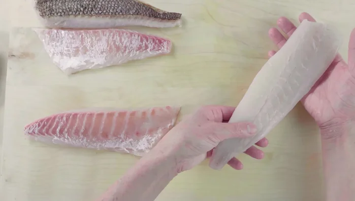 Identify the 'shitami' (bottom half) and 'uwami' (top half) of the fillet. Place the fillet skin-side down on the cutting board with the tail pointing away from you (left side) and the head towards you (right side).