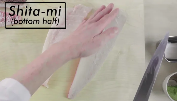Begin slicing the 'shitami' (bottom half) of the fillet from the tail end, keeping the slices at a consistent thickness appropriate for nigiri. The fish should always be facing skin side down.