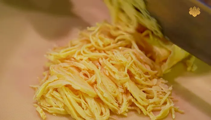 While the omelette cools, roll it into a log and slice into thin strips.