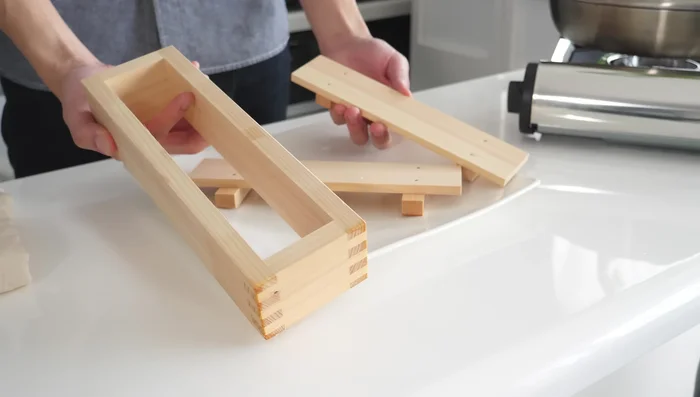 Prepare a container (sushi shaper, milk carton with holes, or tied filter cloth) for shaping the tofu.
