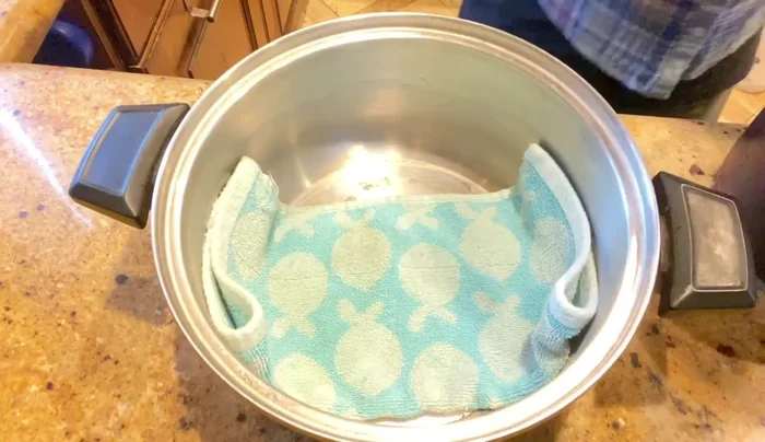 If using a steamer, place the container in the steamer. If using a pot, place a small towel in the bottom of a large pot, place a heat-proof bowl upside down in the pot, add water, and place the container on top of the bowl. Cover with a lid wrapped in a kitchen towel to prevent dripping.