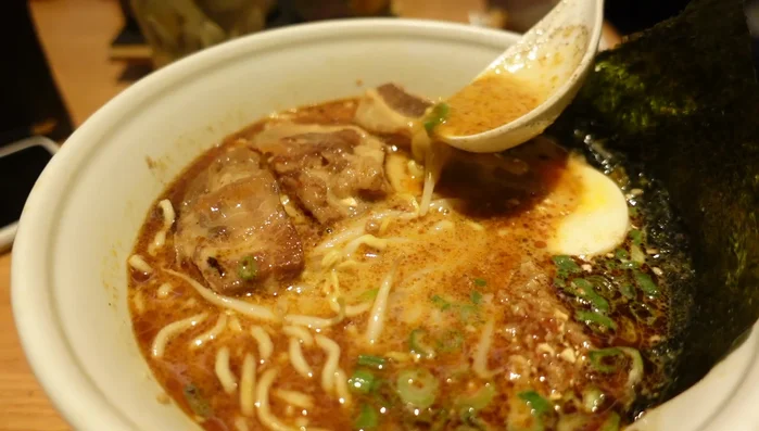 Mix the bean paste into the soup to adjust the spiciness. The speaker mentions that mixing in the bean paste reduces the spiciness.