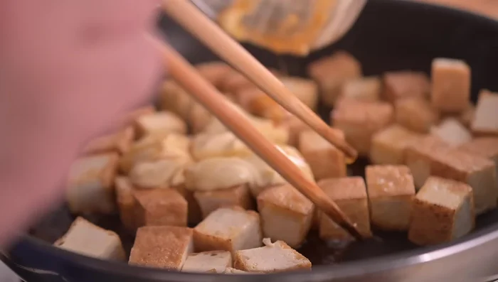 Add the mixed seasonings to the fried tofu in the pan and stir-fry.