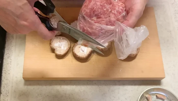 Cut a corner of the meat bag and squeeze the meat mixture into the shiitake mushroom caps, pressing firmly to create a flat surface.