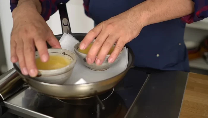 Pour water into the frying pan until it reaches about half the height of the containers.