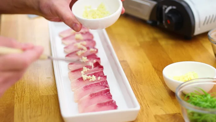 Top Hamachi with minced garlic, ginger slices, and green onion curls.