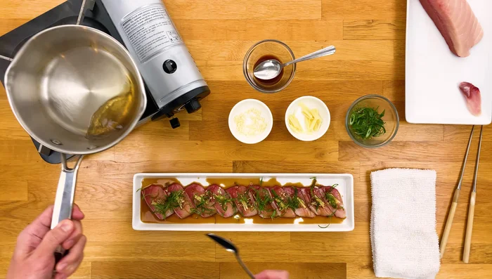 Carefully pour the hot smoking oil over the Hamachi, searing it immediately.