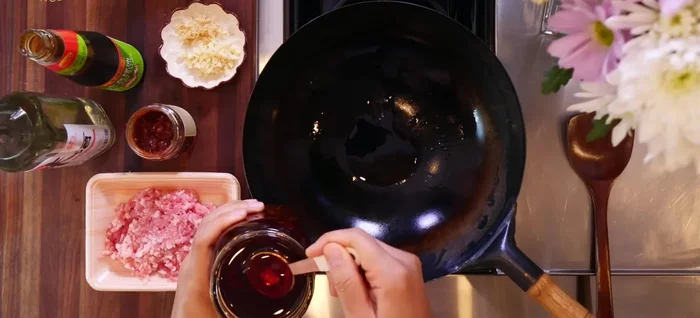 Prepare the pork topping: Heat a wok or skillet over high heat. Add chili oil, garlic, and ginger. Stir-fry for about a minute.