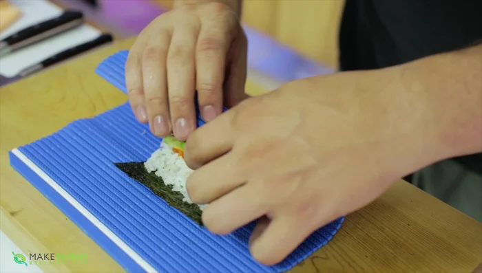 Roll the sushi using a bamboo mat, sealing the edges.