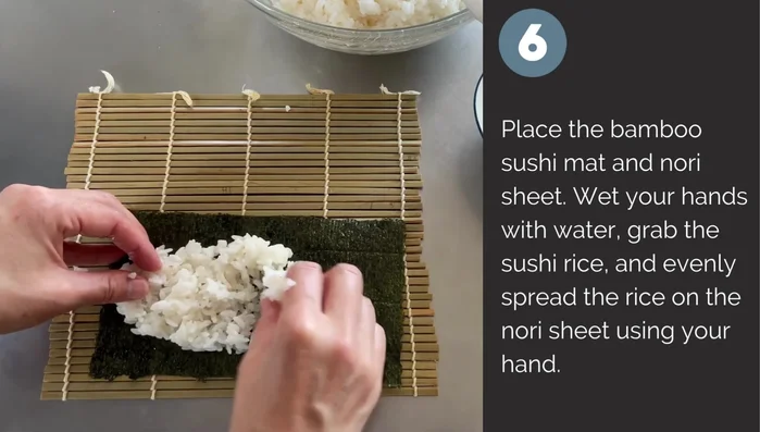 Place bamboo rolling mat, wet your hands, and evenly spread rice on nori sheet.
