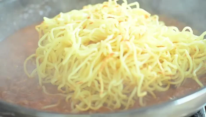 Add the crispy fried noodles to the tomato sauce and mix gently.