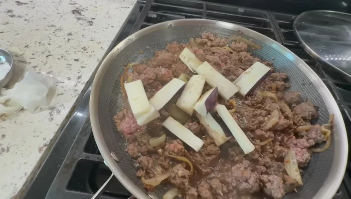 Add the sliced Japanese eggplant to the pan and stir-fry.
